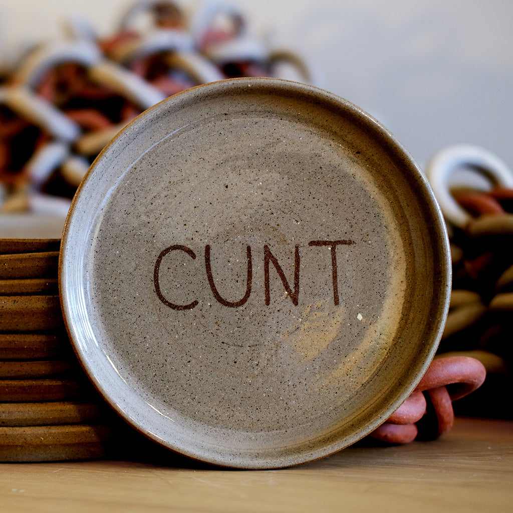 Brown ceramic stoneware 'slur' plate with 'CUNT' written on it.